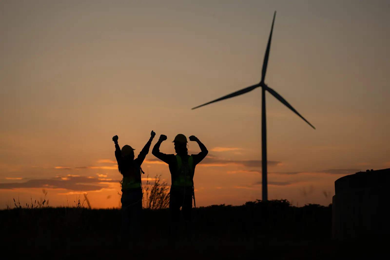 Two technicians celebrating at sunset beside a wind turbine